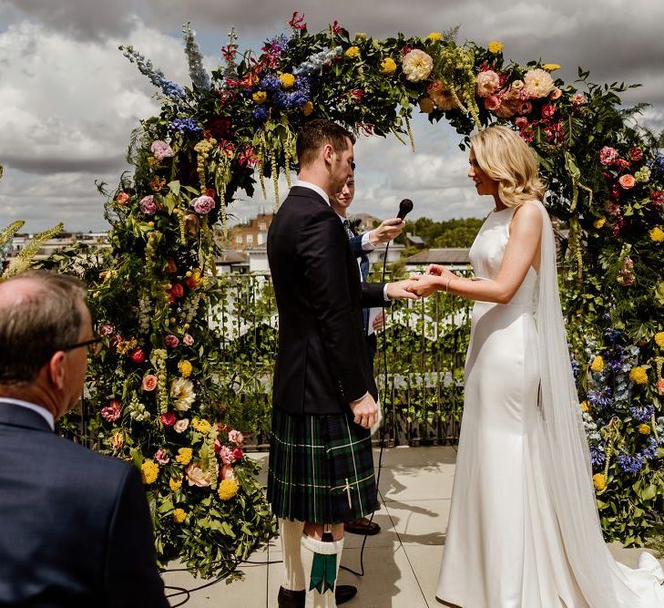 Bride and groom exchange vows at rooftop wedding in London with floral moon gate decor