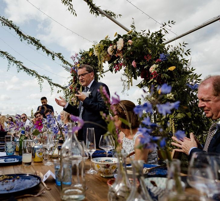 Toasts at outdoor wedding reception with hanging foliage and floral decor