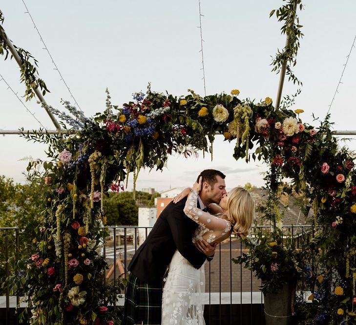 Bride and groom embrace at outdoor reception wearing beautiful bridal jumpsuit