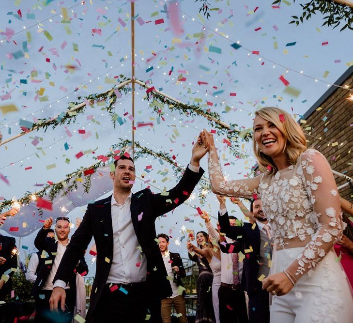 Bride wearing bridal jumpsuit at outdoor celebration with multi-coloured confetti and floral decor