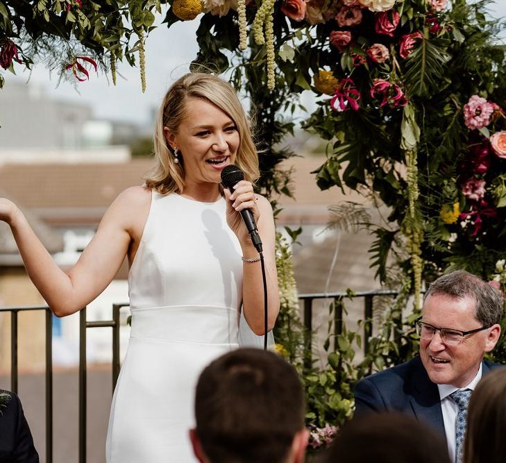 Bride enjoying the speeches at rooftop wedding with floral decor