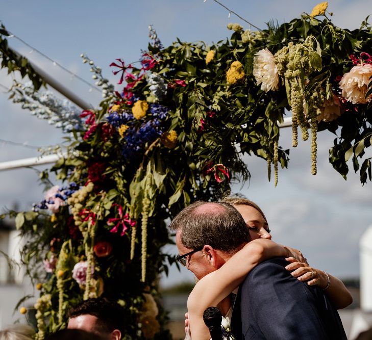 Bride hugs family member at outdoor wedding with floral decor