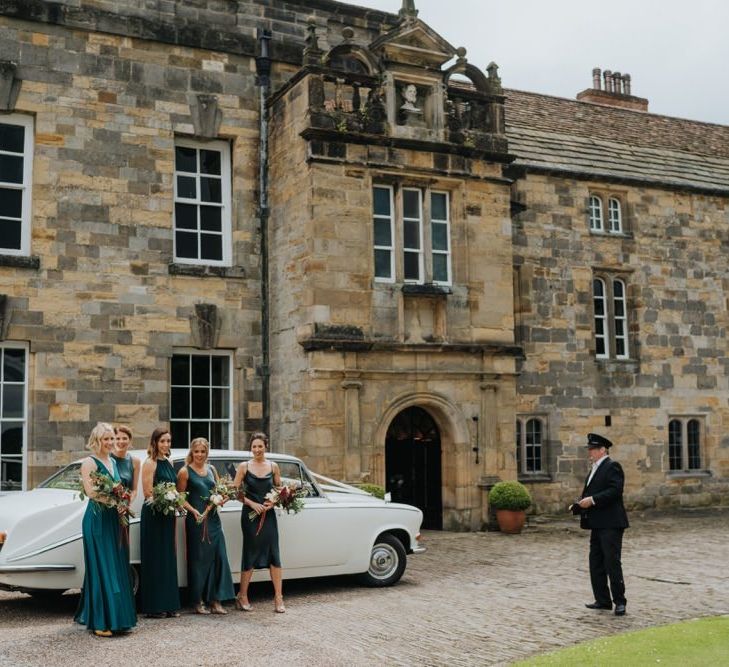 Bridesmaids wearing emerald green dresses at country house wedding ceremony with vintage car