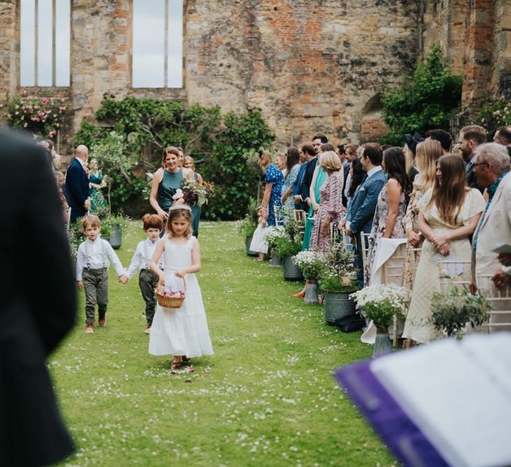 Flower girl walking down the aisle at outdoor ceremony with olive trees