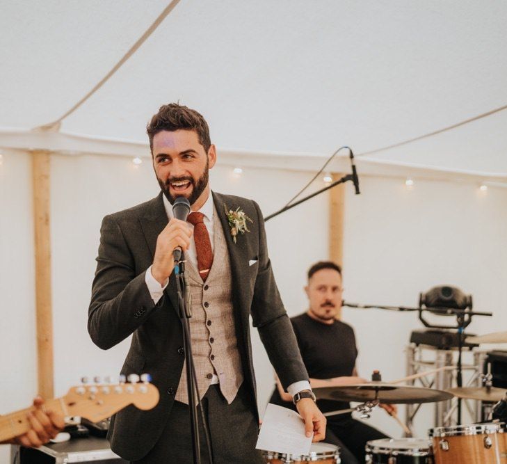 Groom wearing three piece suit and red tie at marquee reception