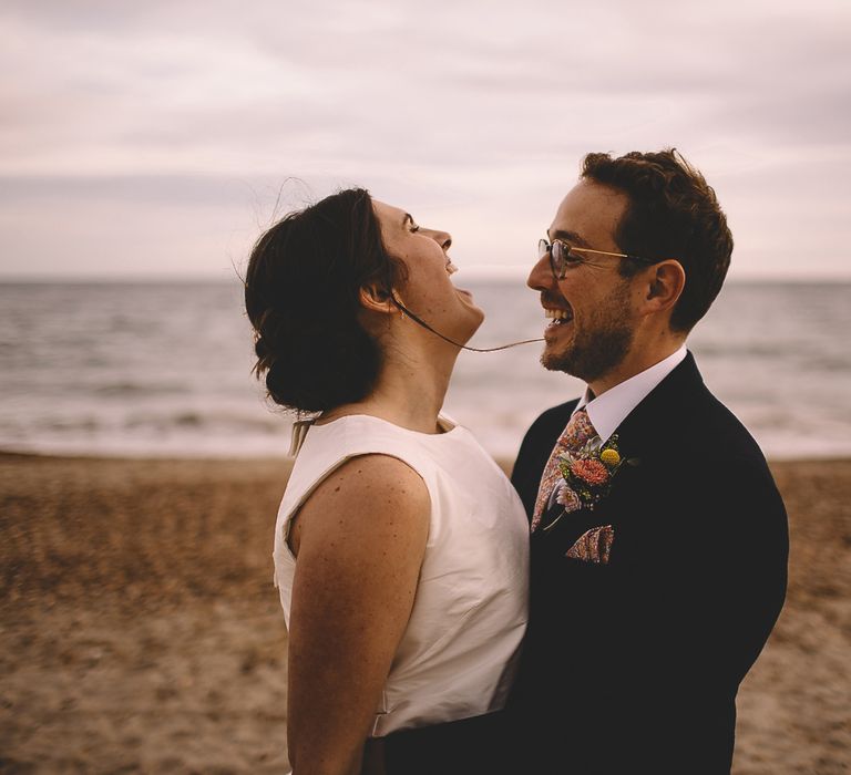 Bride in Homemade Wedding Dress with Bow Back and Groom in Dress2Kill Suit Laughing on the Beach