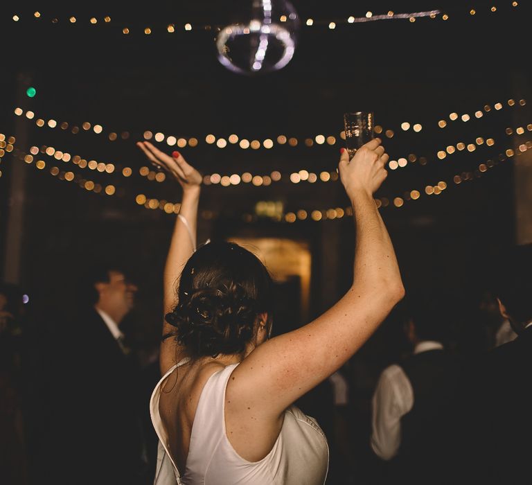 Bride in Homemade Wedding Dress with Bow Back Detail Dancing at Evening Reception with Fairylight Backdrop