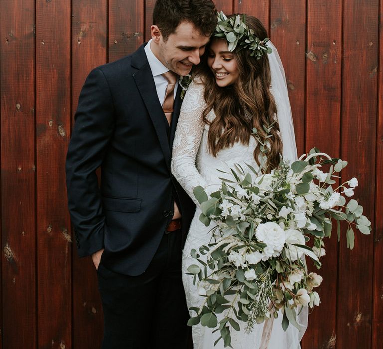 Bride Long Sleeve Grace Loves Lace Wedding Dress and Groom in Moss Bros. Suit Embracing