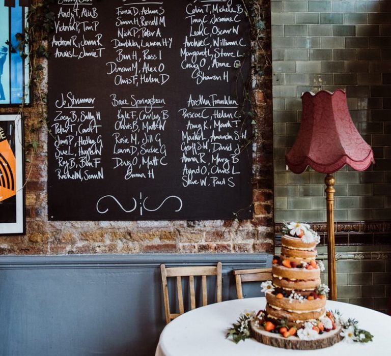 Chalkboard table plan at pub reception with naked wedding cake decorated with berries