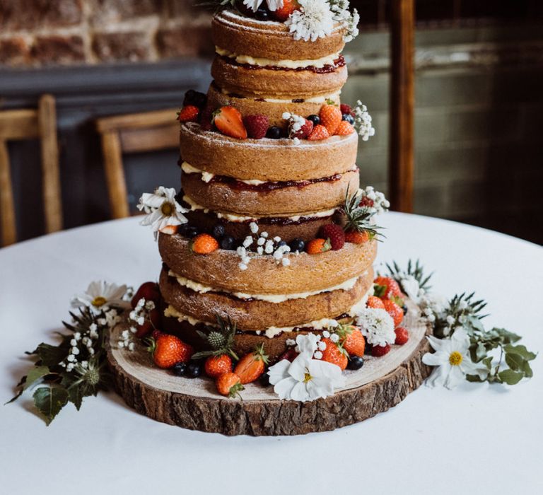 Naked wedding cake with berry and floral decorations on rustic tree stump stand