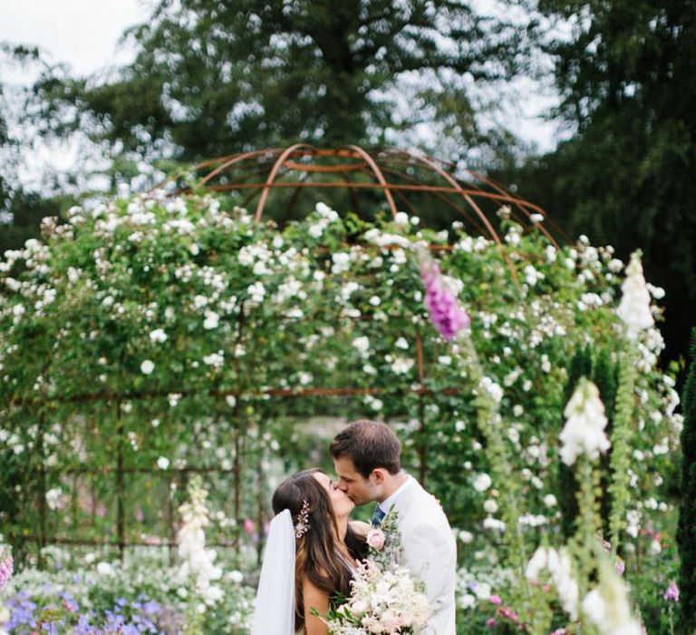 Bride and Groom Kissing in the Gardens Surrounded by Flowers