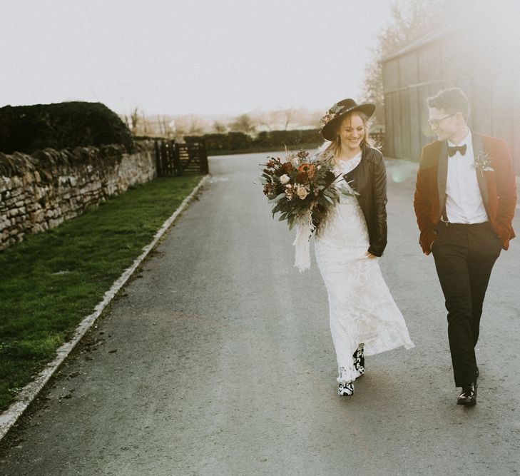 Golden Hour Portrait of Bride in Phase Eight Wedding Dress, Fedora Hat, Boots and Leather Jacket with Groom in Red Velvet Tuxedo Jacket