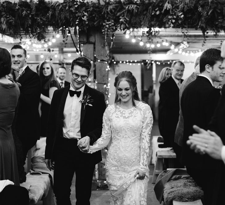 Bride in Phase Eight Wedding Dress and Groom in Tuxedo Walking Into Their Wedding Reception