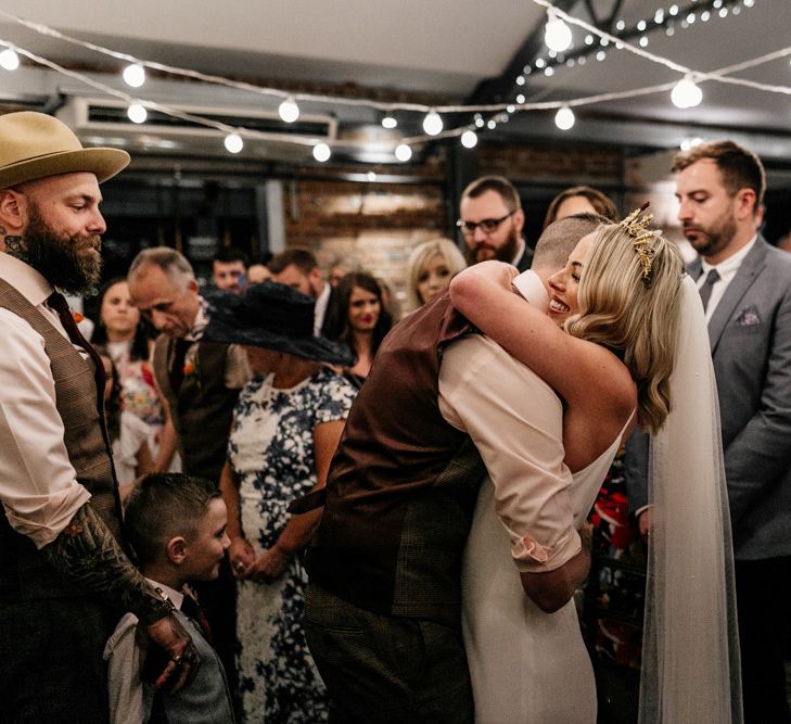 Bride and groom hugging under festoon lights.