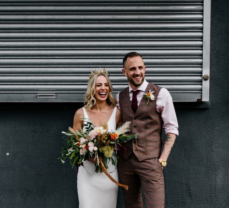 Bride in minimalist wedding dress and gold bridal crown and groom in brown check waistcoat