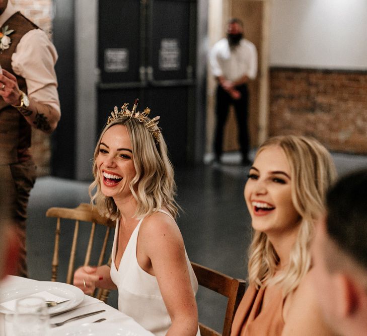 bride in gold crown smiling at wedding speeches