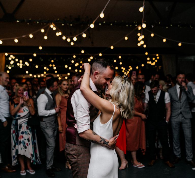 Stylish bride and groom in slip wedding dress, gold bridal crown and waistcoat taking their first dance