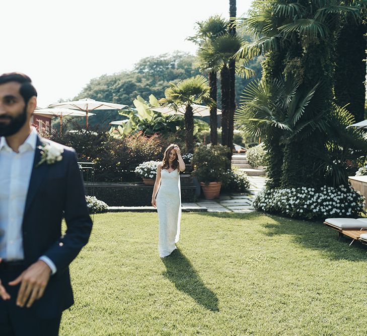 Bride in Grace Loves Lace Wedding Dress Approaching Groo in Navy Suit for First Look