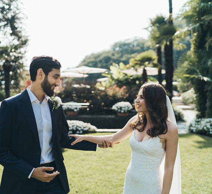 Bride in Grace Loves Lace Wedding Dress Approaching Groom in Navy Suit for First Look