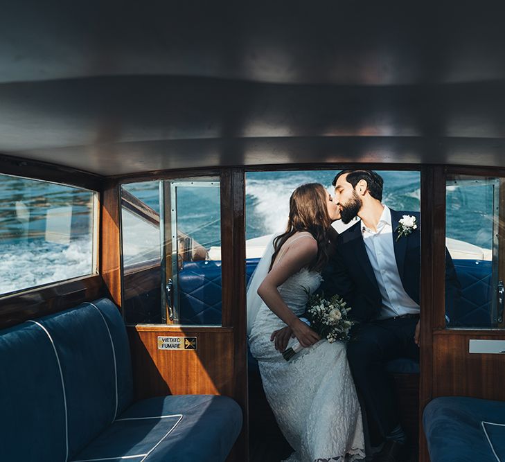 Bride in Grace Loves Lace Mia Wedding Dress and Groom in Taliare Navy Suit Kissing on Boat Ride Over Lake Como