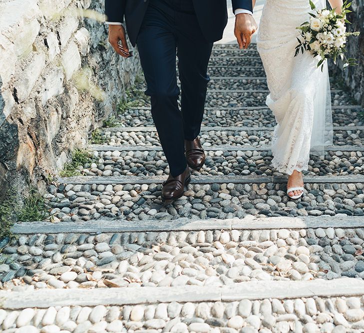 Groom in Navy Suit with Monk Strap Shoes and Bride in Lace Wedding Dress with Strappy Sandals