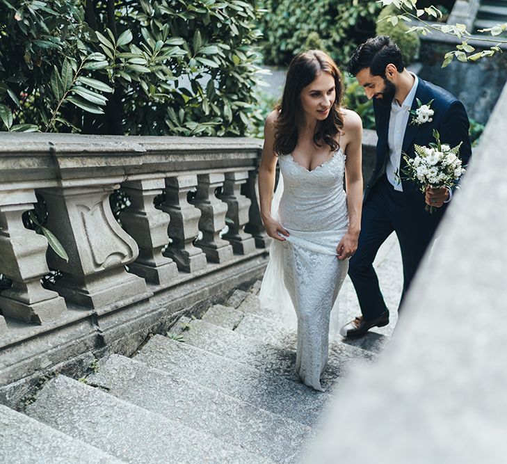 Bride in Grace Loves Lace Mia Wedding Dress and Groom in Taliare Navy Suit Walking up Steps