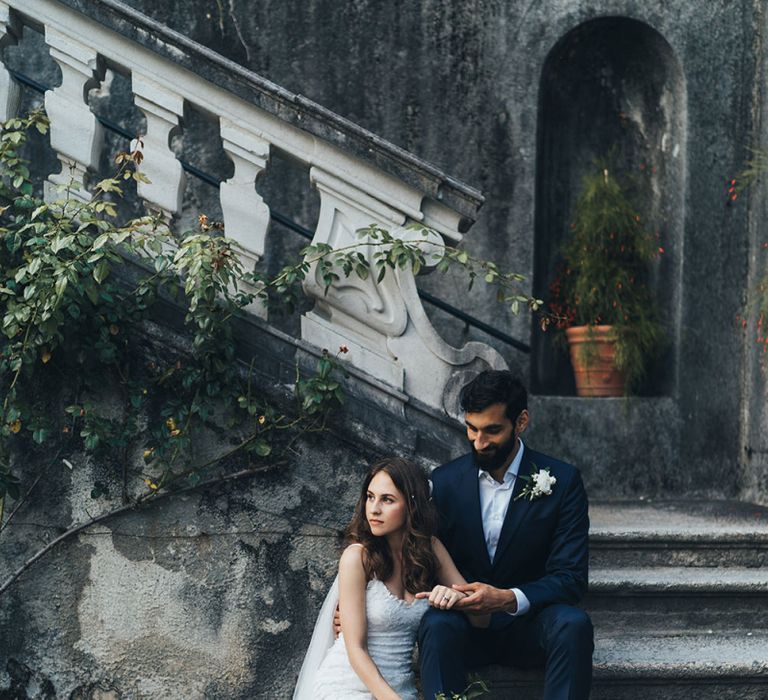 Bride in Grace Loves Lace Mia Wedding Dress and Groom in Taliare Navy Suit Sitting on Steps