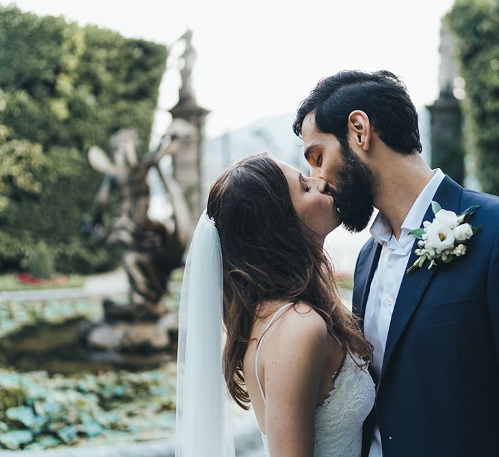 Bride in Grace Loves Lace Mia Wedding Dress and Groom in Taliare Navy Suit  Kissing in Garden