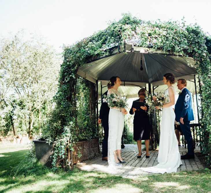 Outdoor wedding ceremony with bride in appliqué wedding jumpsuit and bride in embellished low back dress