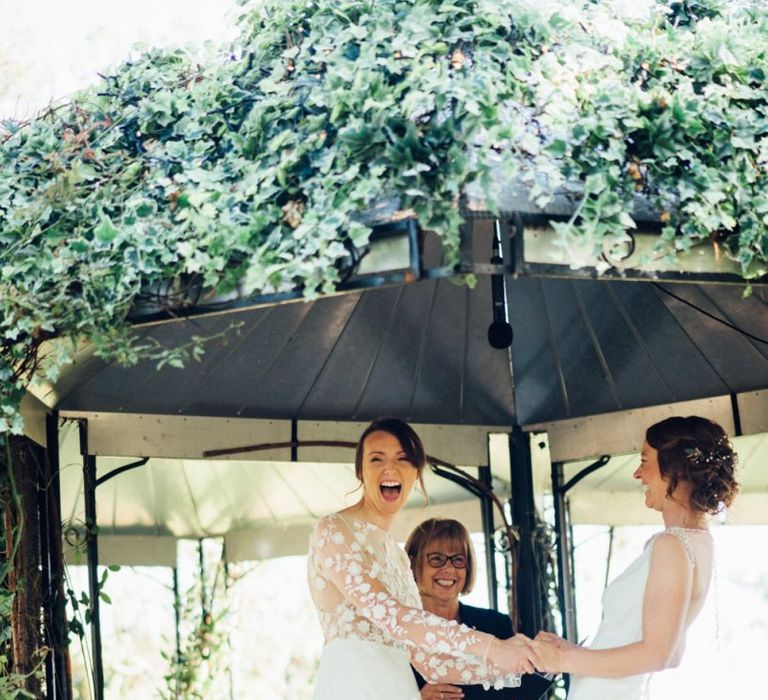 Outdoor wedding ceremony with bride in appliqué wedding jumpsuit and bride in embellished low back dress