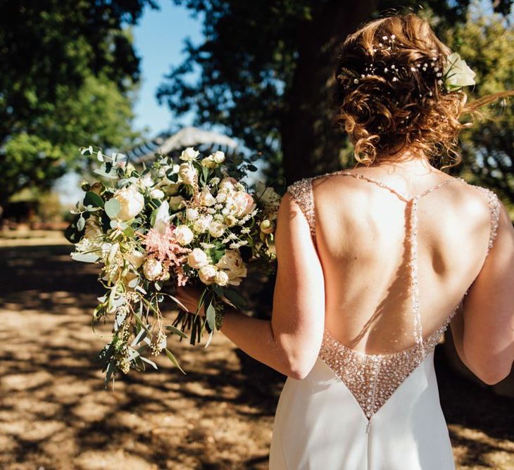 Bride wearing low back embellished dress with beautiful white and dusky pink wedding bouquet at woodland autumn wedding