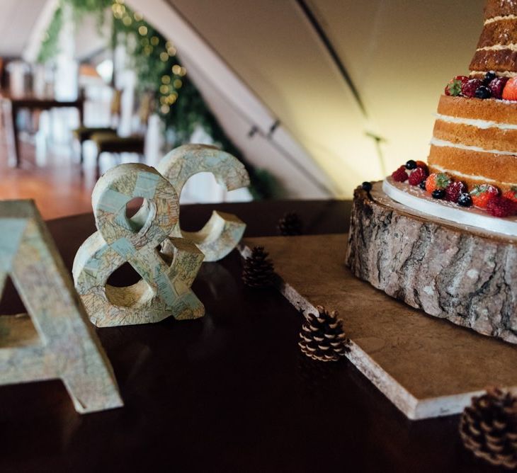 Personalised letter signs next to naked  cake with pinecones at woodland celebration