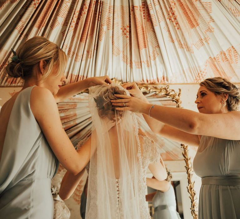 Bridesmaids in green dresses help bride position her veil