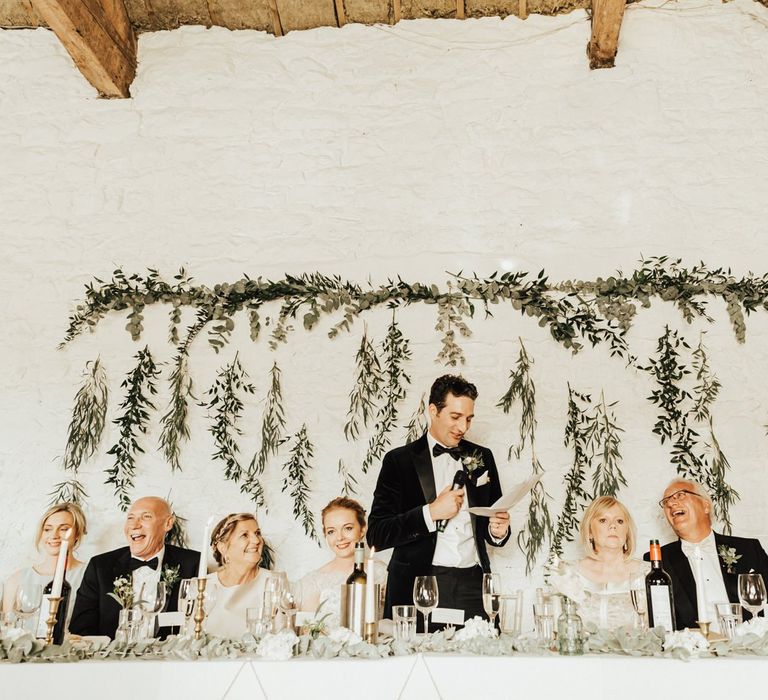 Groom wedding speech in front of hanging foliage decor