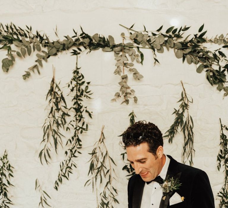 Groom wedding speech in front of hanging foliage decor