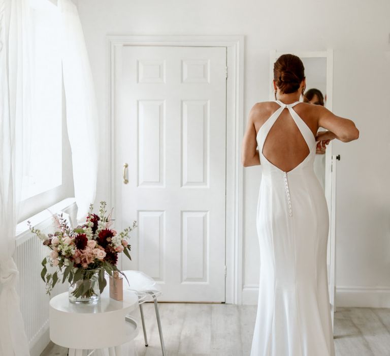 Bride on wedding morning putting on a halter neck dress