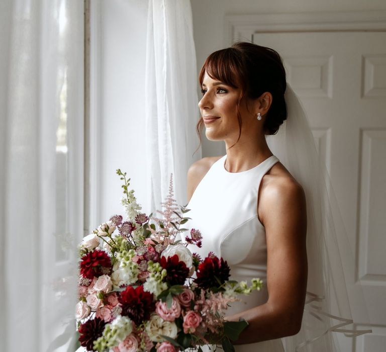 Bride in minimalist wedding dress holding a pink and red bouquet