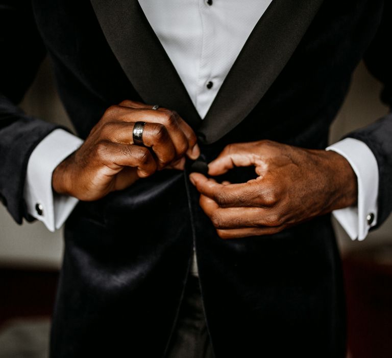 Groom tying up the buttons on his blue velvet jacket