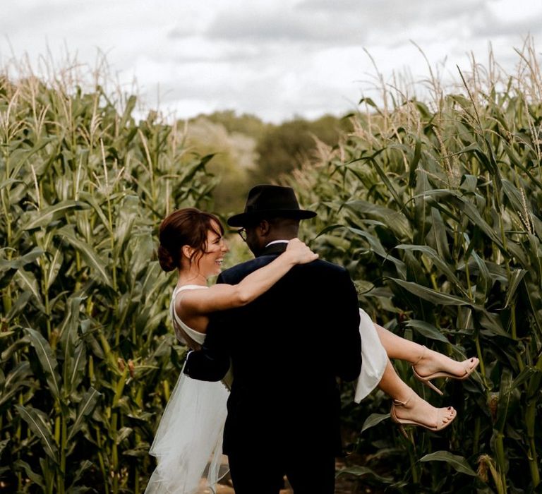 Stylish groom in velvet dinner jacket and Fedora hat picking up his bride