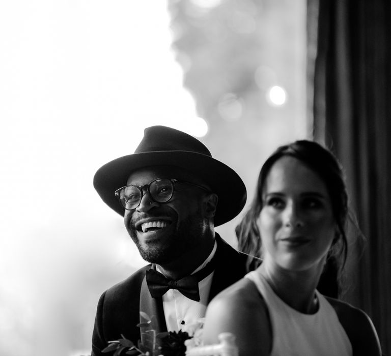 Stylish groom in Fedora hat smiling during the wedding reception speeches