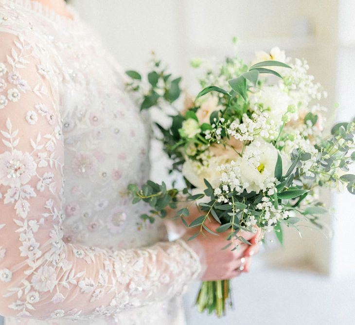 Bride in Needle and Thread Embellished Wedding Dress with Long Sleeves Holding a White and Green Wedding Bouquet