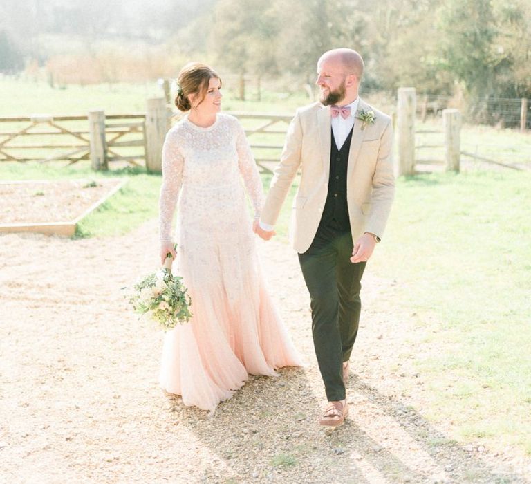 Bride in Needle &amp; Thread Wedding Dress and Groom in Beige Blazer and Pink Bow Tie Holding Hands