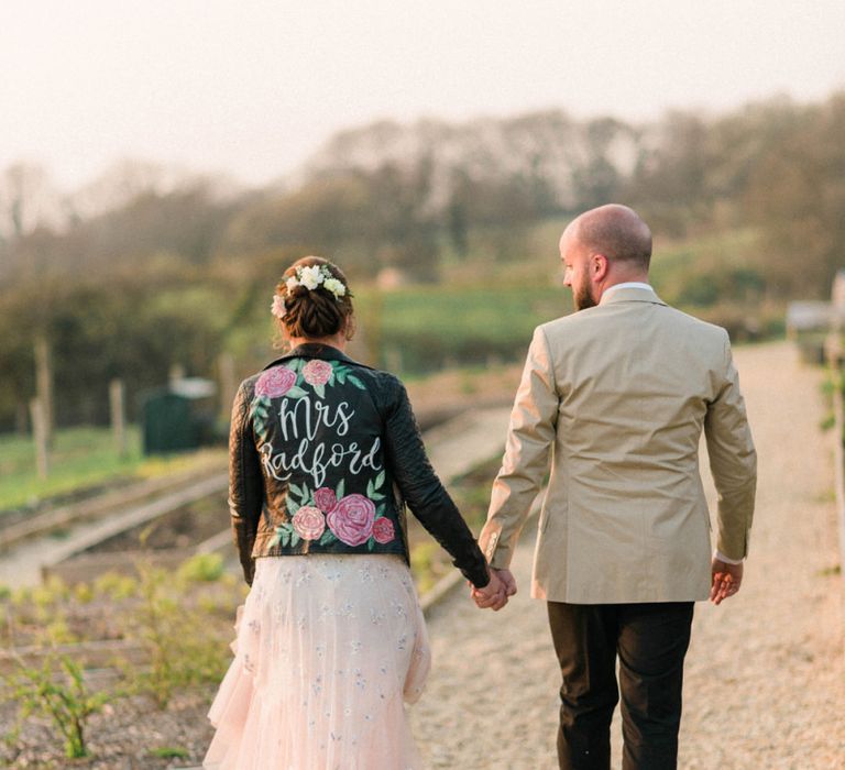 Groom in Black Trousers and Beige Blazer and Bride in Hand Painted Leather Jacket Hand in Hand