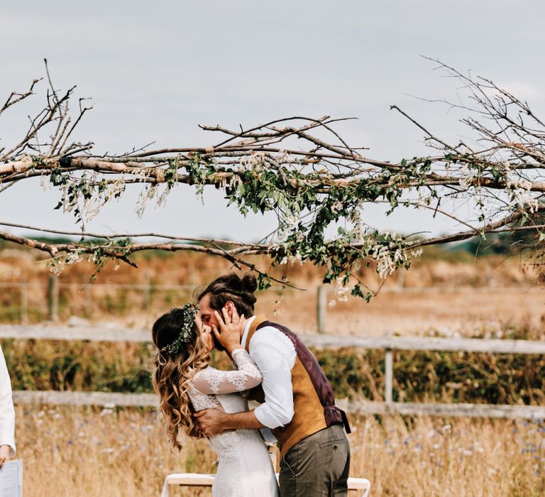 Bride and groom kiss under wooden wedding arch