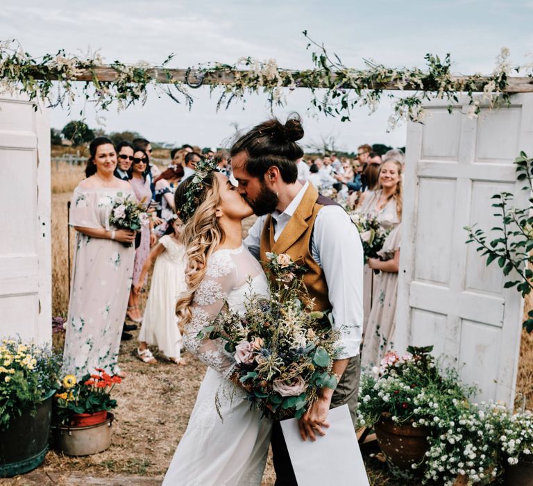 Bride and groom kiss at outdoor ceremony with rustic decor and  globe guest book