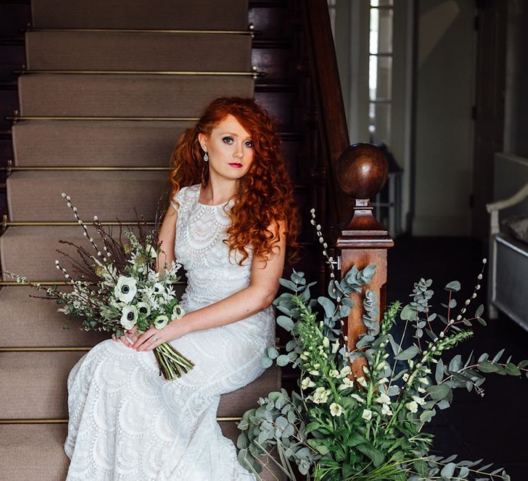 Bride in Lace Wedding Dress Sitting on Stairs with Floral Arrangement and Anemone Bouquet