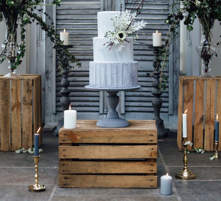 Grey and White Wedding Cake Stood on Wooden Crate with Floral Arrangements