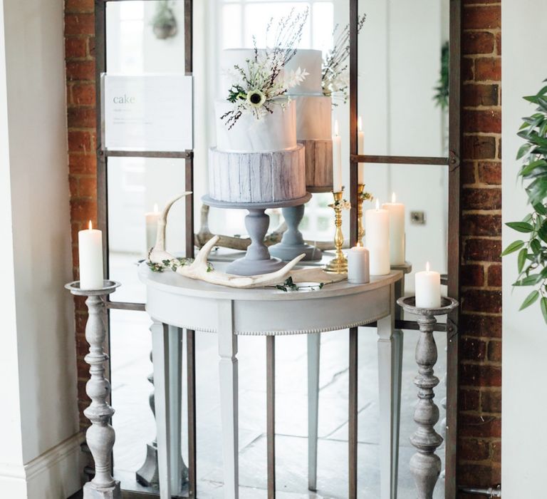 Grey and White Wedding Cake Displayed on Table in Front of Large Window Pane Mirror