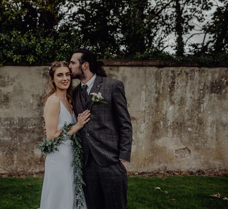 Boho Bride in High Low Slip Wedding Dress and Ivy Garland with Groom in Brown Check Suit Embracing