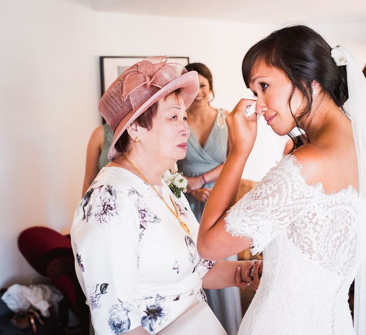 Bride in Lace Watters Dress with Bardot Neckline and Buttons Down Back | Blossom and Bluebird Cathedral Length Veil | Bridal Up Do | Bridesmaids in Sage Green Dresses with Embellished Straps from ASOS | Mother of the Bride in White Floral Dresses with Pink Hat | Smoke Bombs and Chinese Paper Fans Backdrop with Bride in Bardot Dress | Twig &amp; Vine Photography